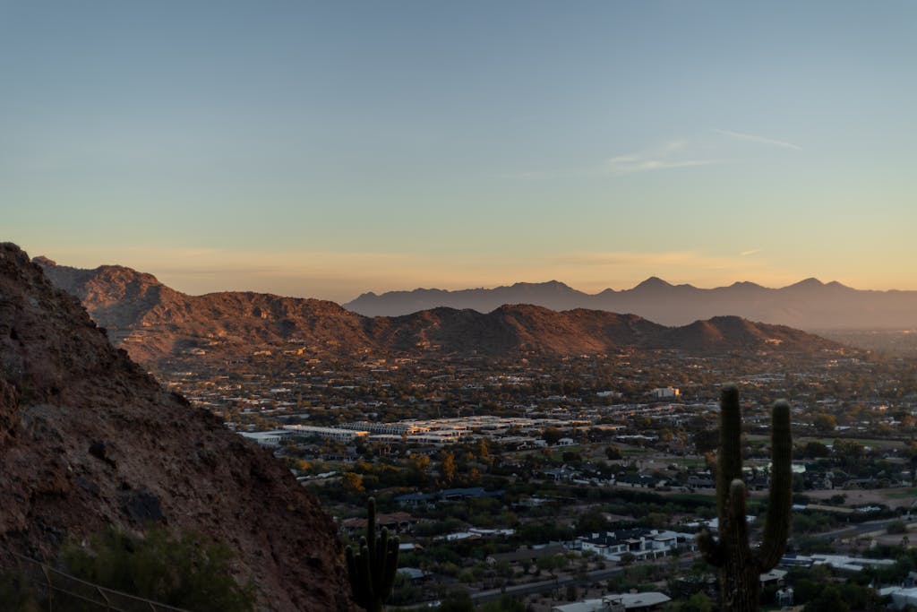 Breathtaking view of Phoenix cityscape and desert mountains at sunset with silhouetted cacti.