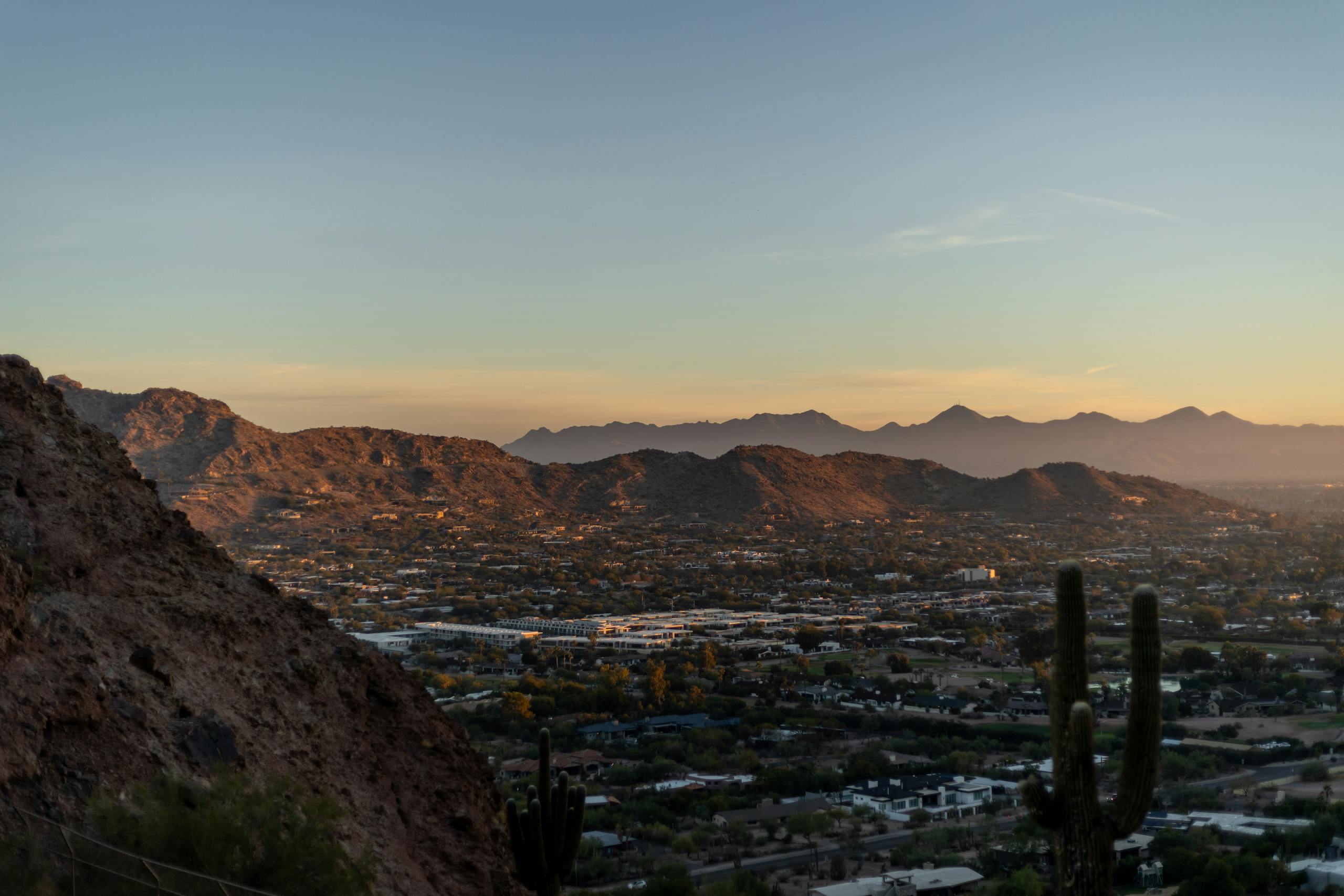 Breathtaking view of Phoenix cityscape and desert mountains at sunset with silhouetted cacti.